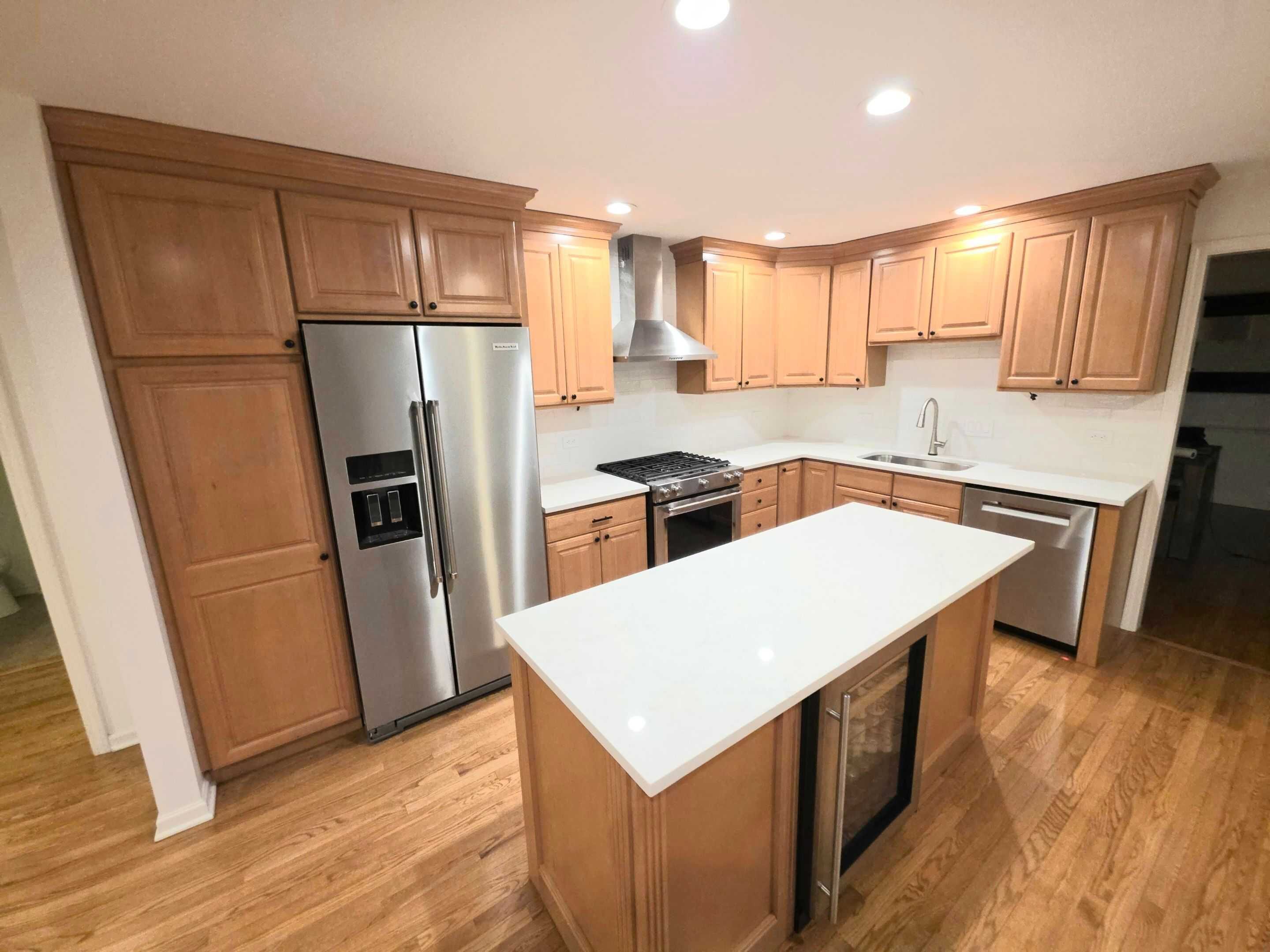 White quartz island and perimeter countertops in a kitchen with maple cabinets and stainless appliances