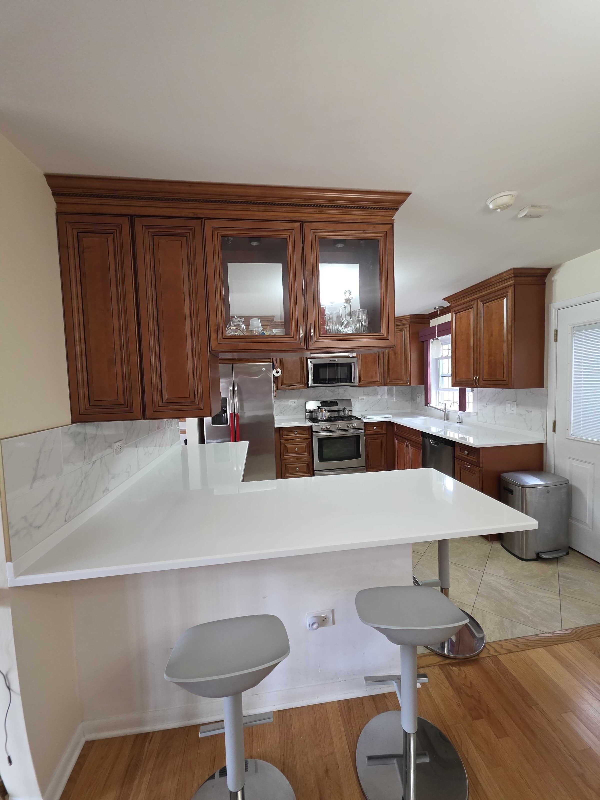 Finished white quartz peninsula with two stools, cherry cabinets and a tiled floor