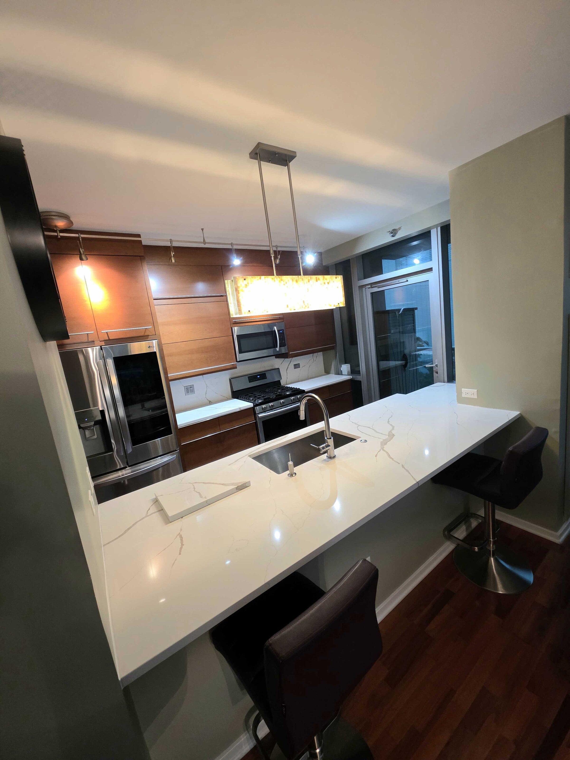 Finished calacatta-look quartz breakfast bar running the length of a walnut condo kitchen