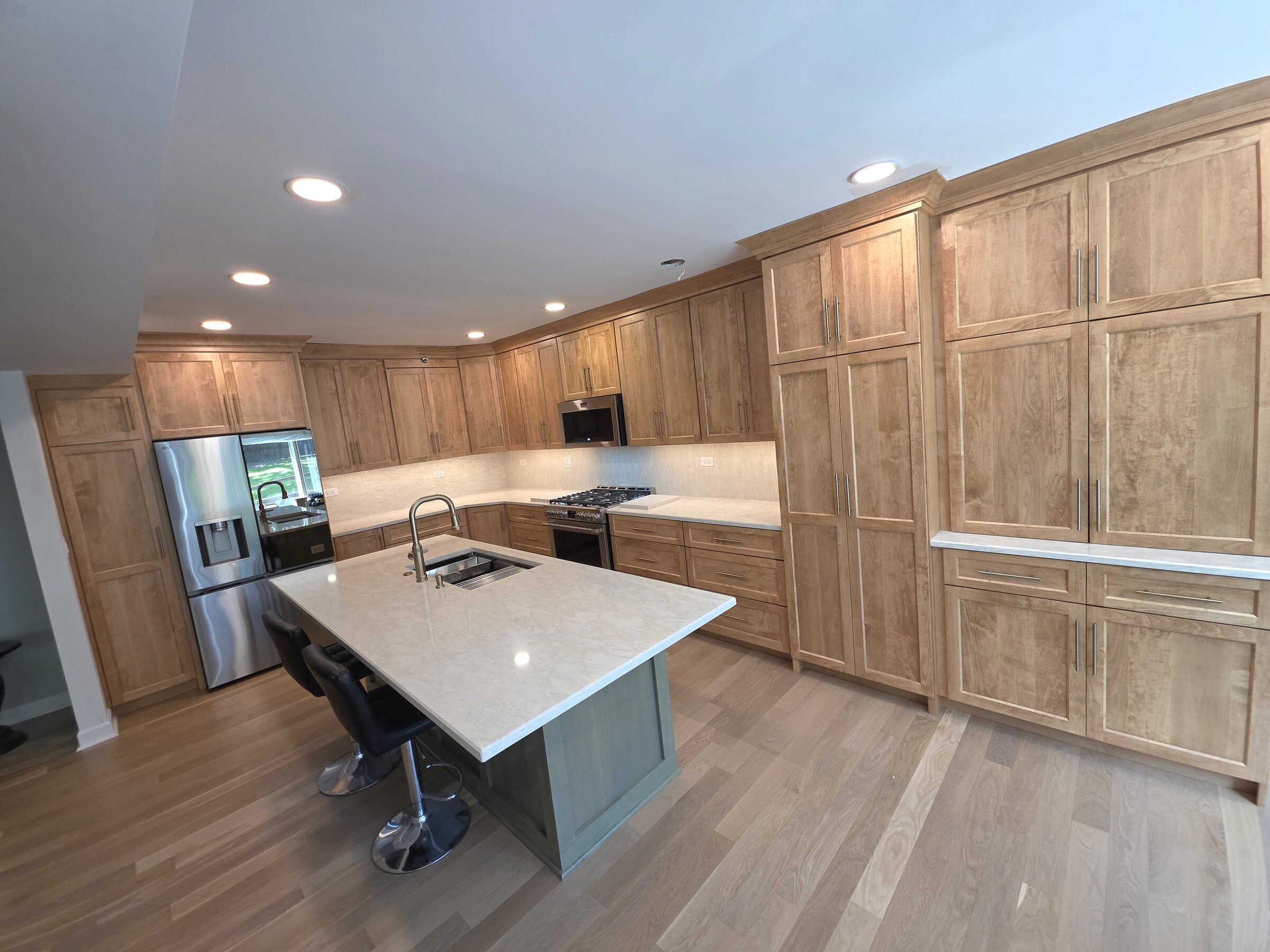 Wide view of the finished kitchen, maple cabinetry running wall to wall past the island