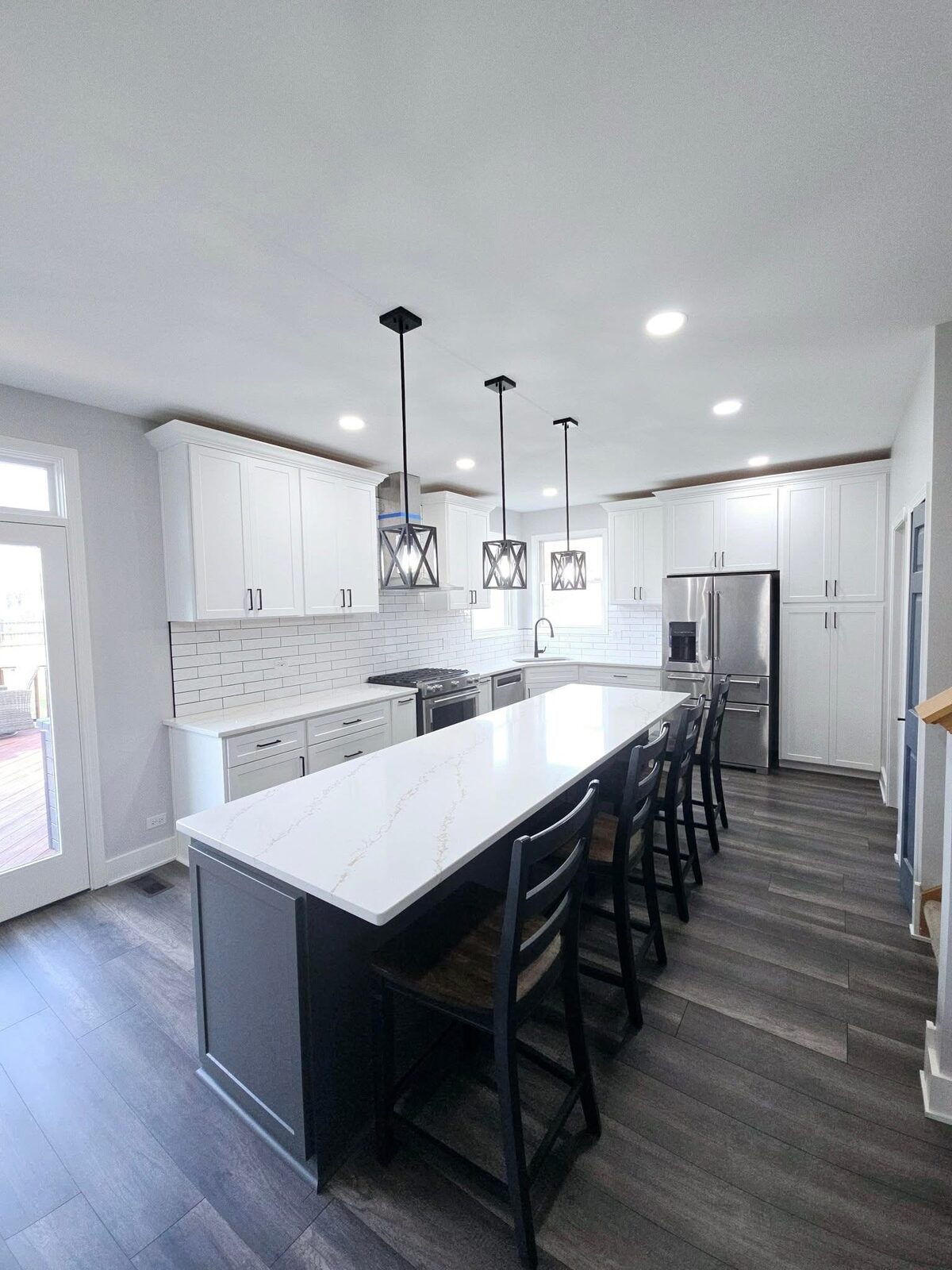 The finished kitchen looking toward the patio doors, stools tucked under the quartz