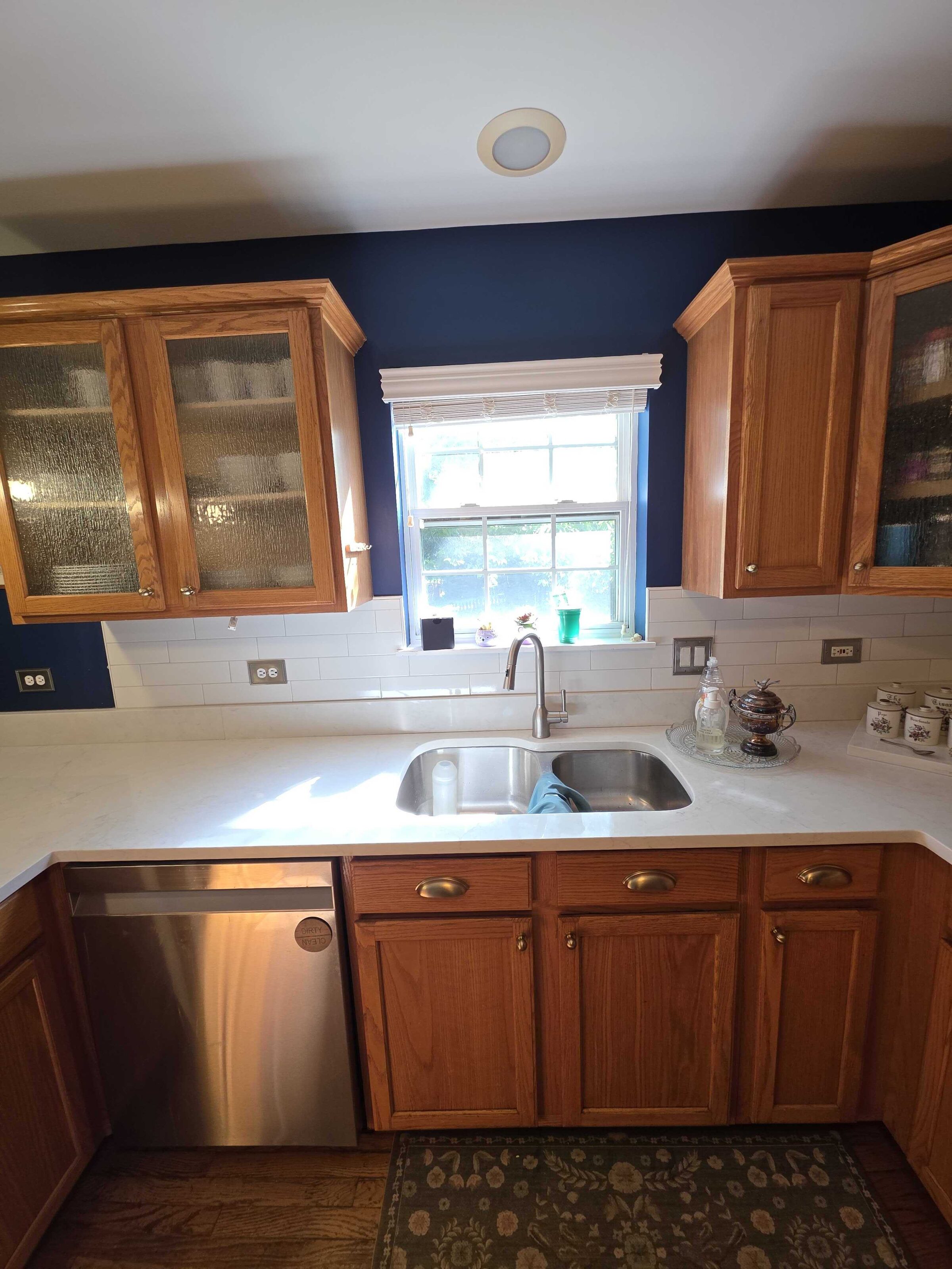 Finished quartz at the sink under a double window, dishwasher panel to the left