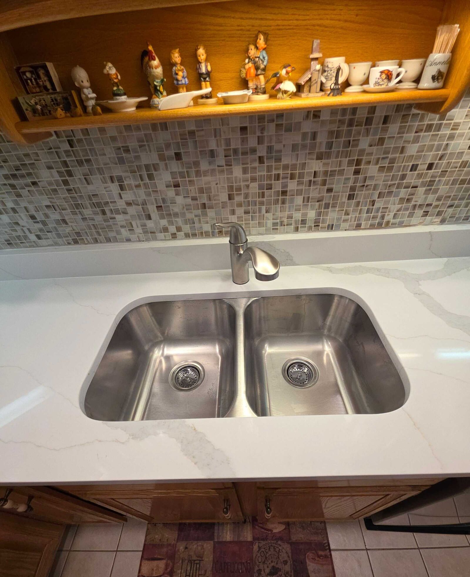 New stainless undermount sink set into white quartz, with the mosaic backsplash and plate rail above