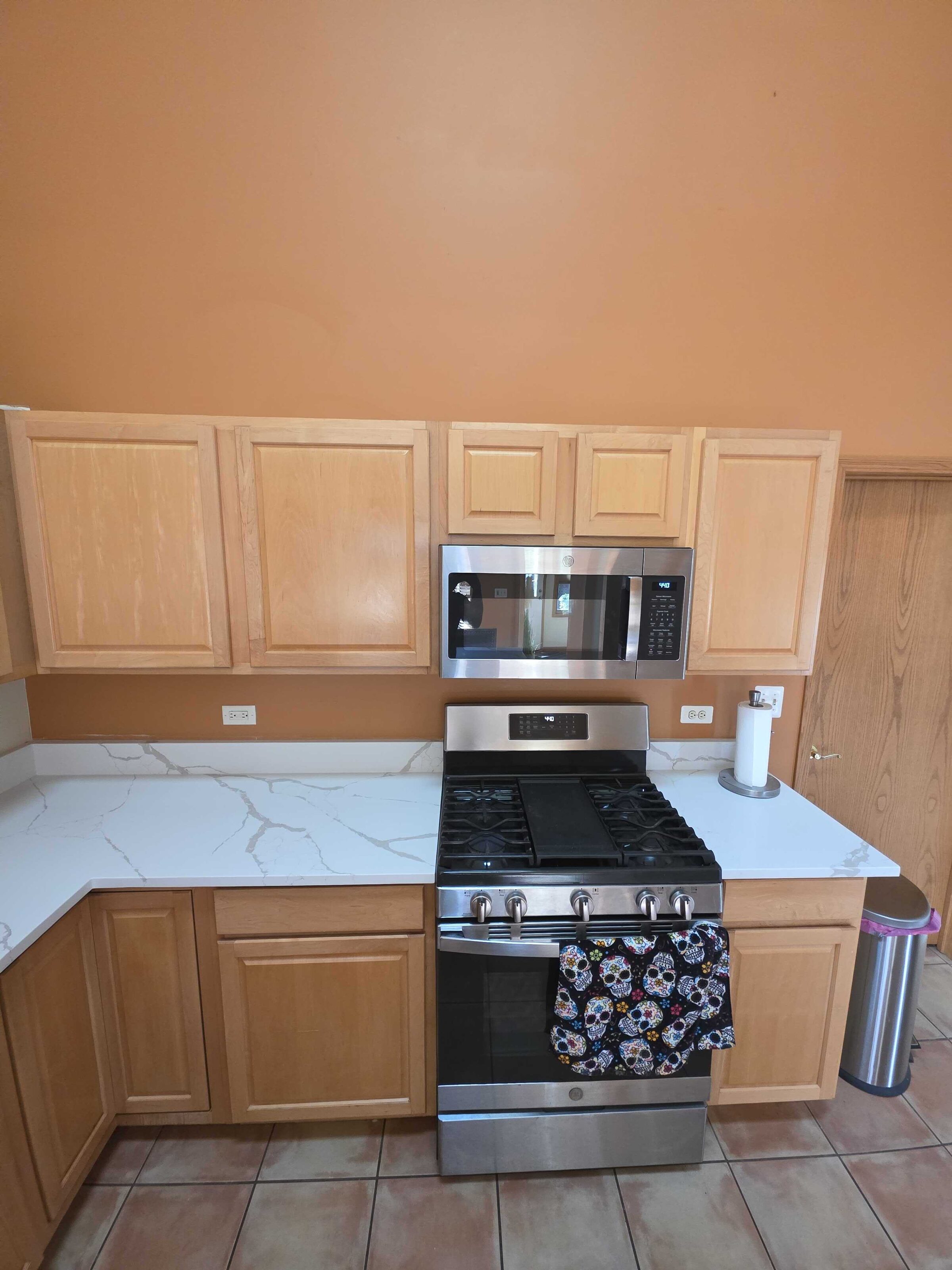 Veined white quartz beside the stainless range, oak cabinets above and terracotta tile below