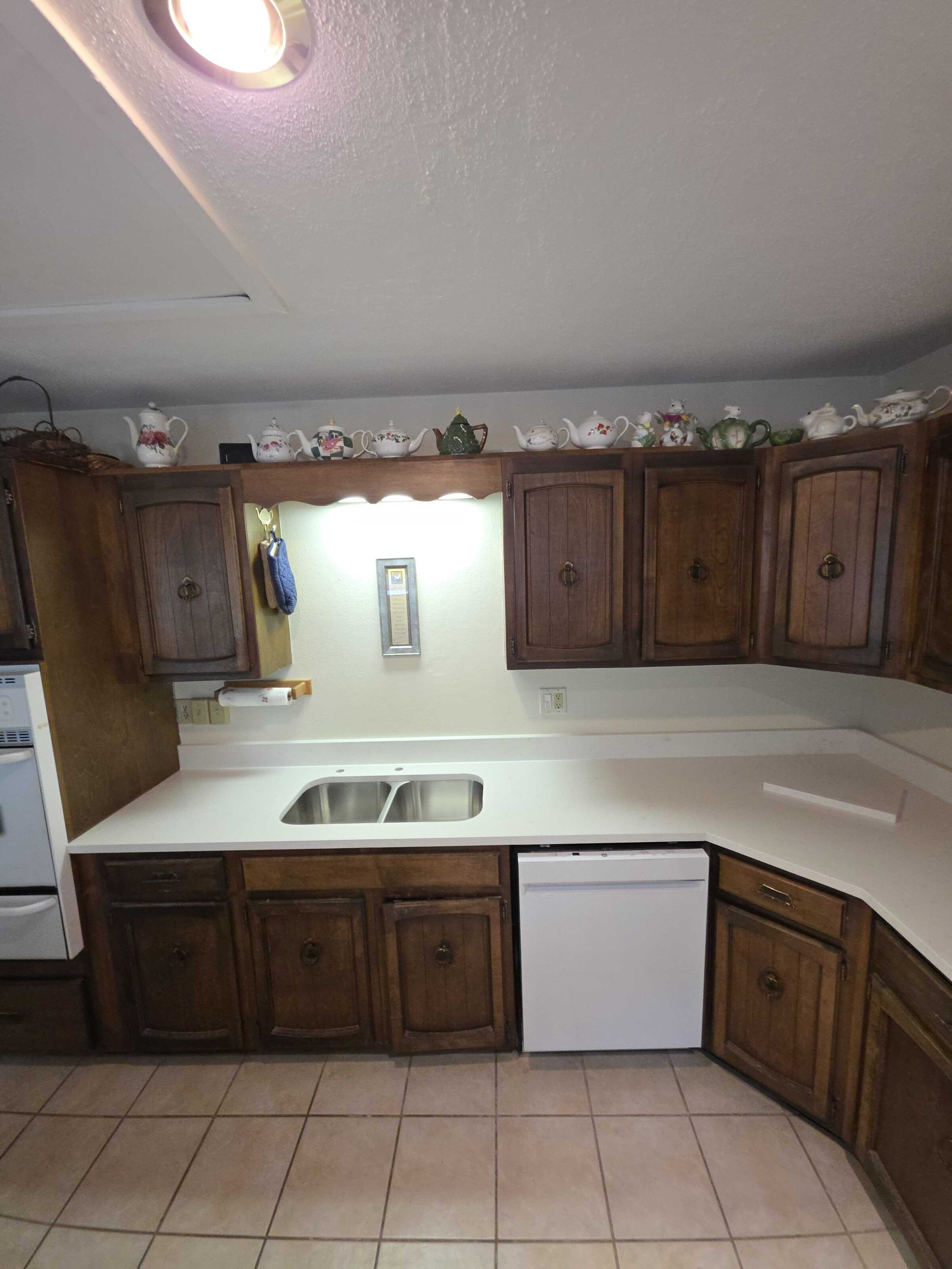 Finished white quartz along the sink run of a dark oak kitchen, with a drop-in stainless sink