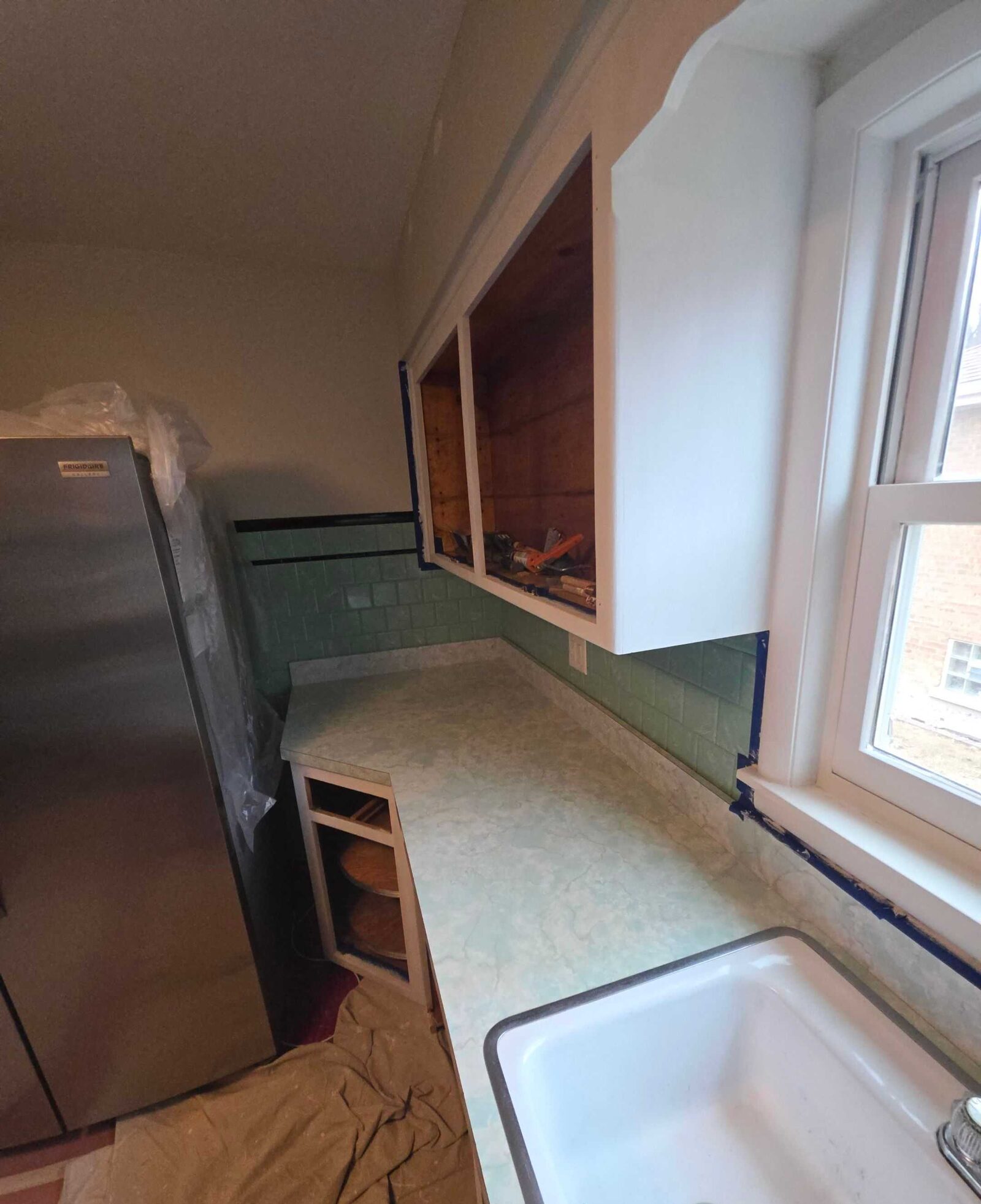 The same corner mid-job: the old apron sink still in place, cabinet doors off and the floor under drop cloths