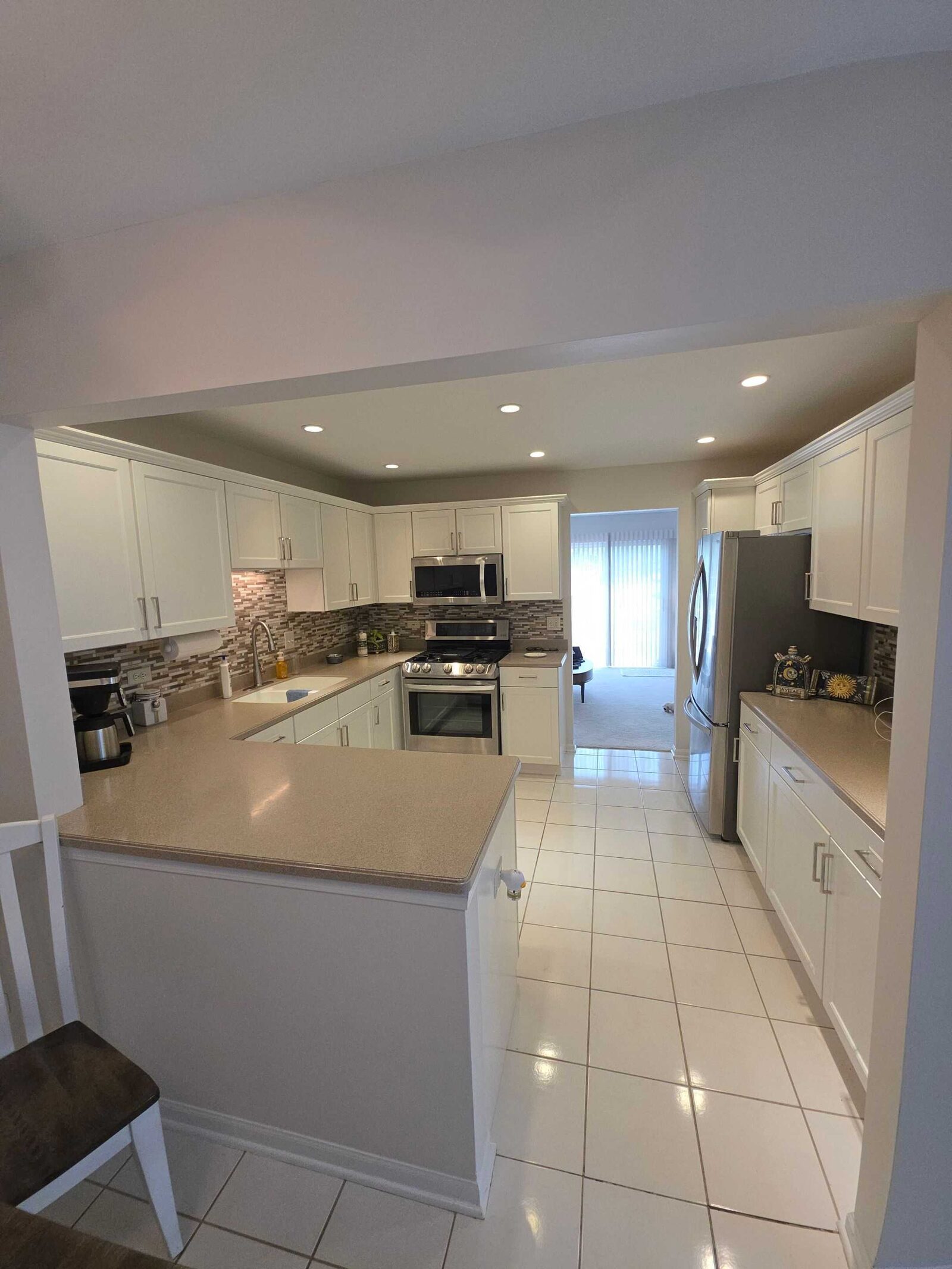The same kitchen before, its beige counter and brown mosaic backsplash pulling warm against white cabinets