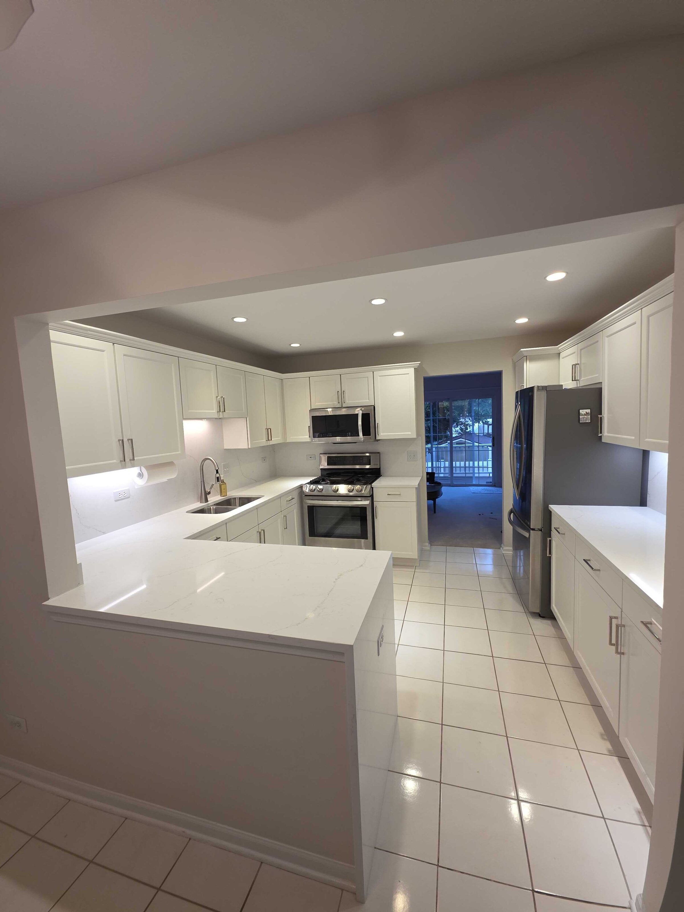 Finished white quartz peninsula and runs in an all-white kitchen with a tiled floor