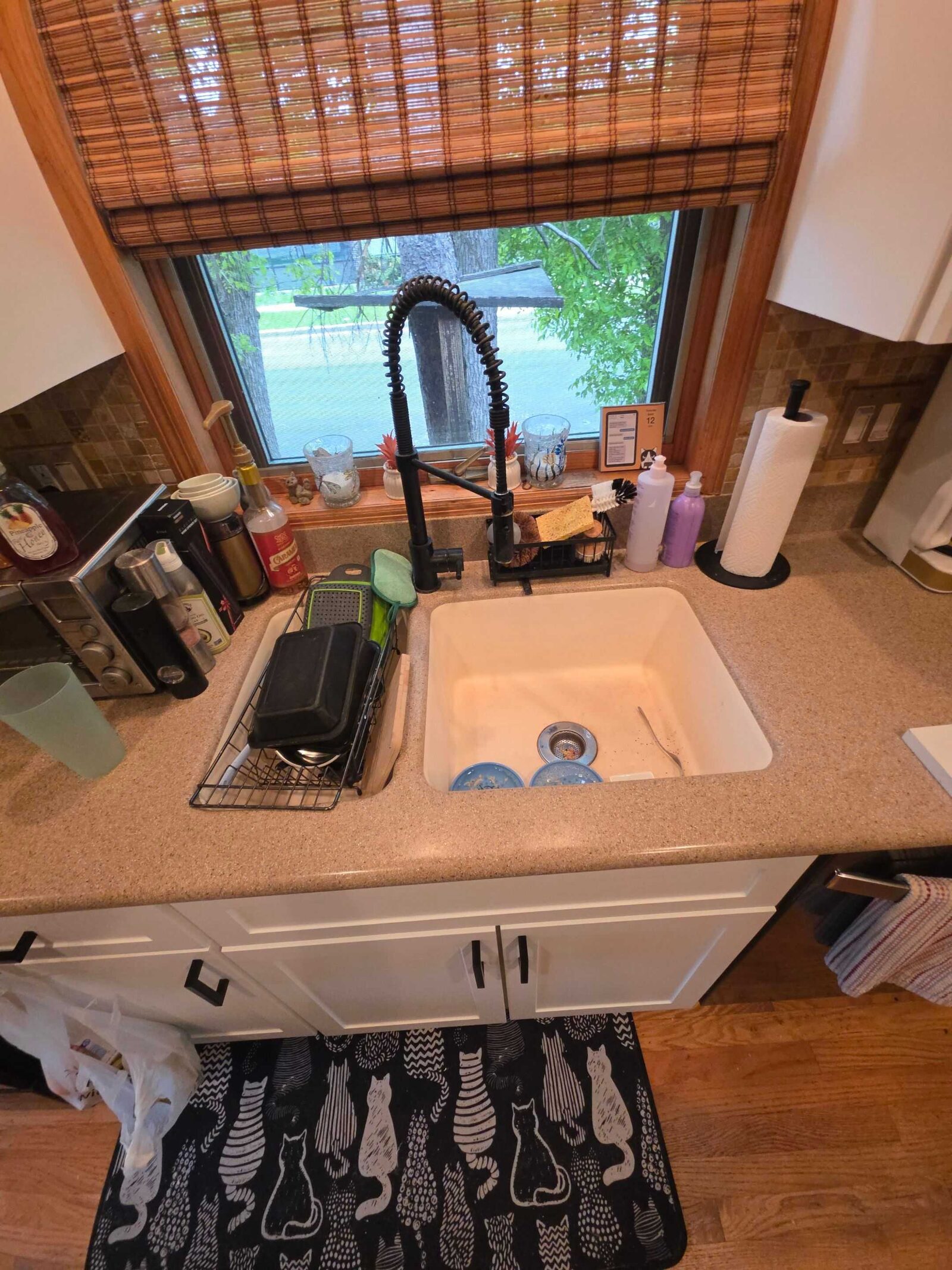 The old tan speckled counter at the sink, with a molded basin and a dish mat alongside